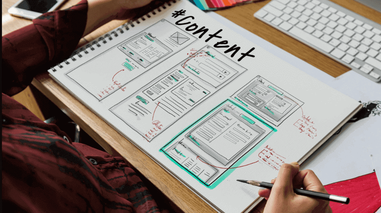 A person sketching website wireframes in a notebook with the word '#content' written at the top